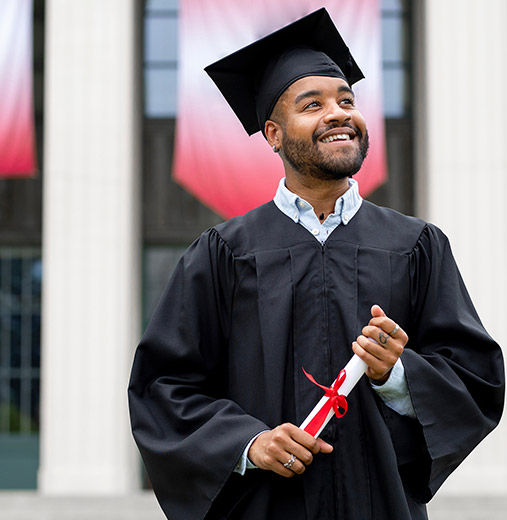 A young African American man smiles while wearing a black graduation cap and gown.