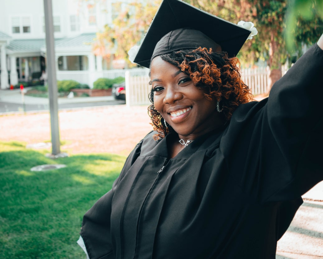 A Black woman wears a black graduation cap and gown while she smiles for a picture.