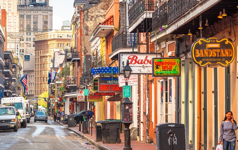 A photo of New Orleans' Bourbon Street photo with bars, stores and buildings on each side of the street.